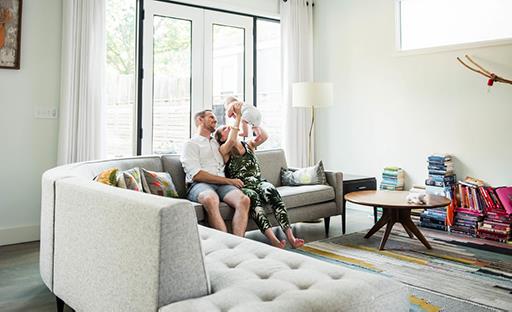 Young couple holding up young baby sitting on couch in living room