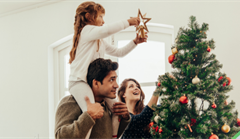 Young couple's daughter placing star on top of Christmas tree